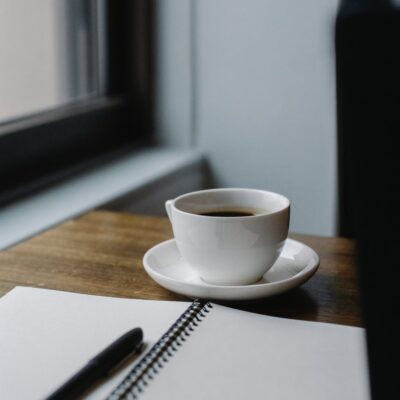 cup of coffee served on table with notepad and pen